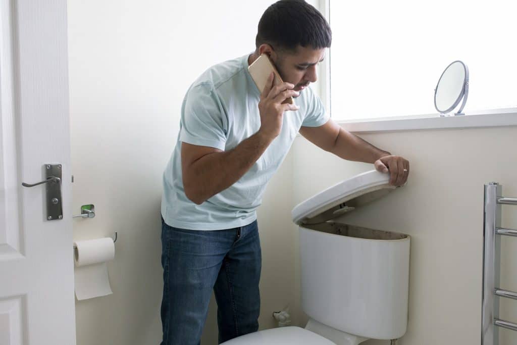 Man looking into a backed up toilet's sewer line